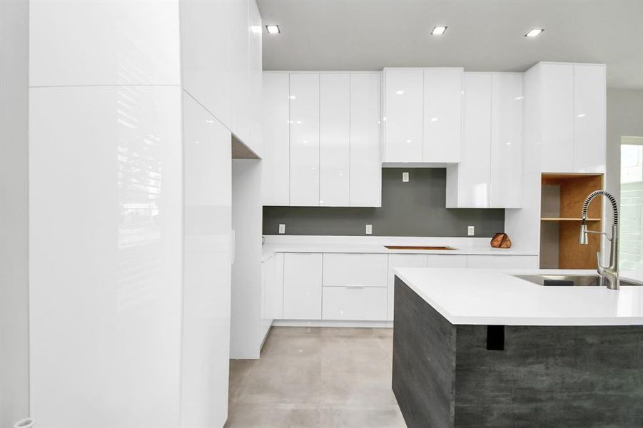 Modern kitchen featuring sleek white cabinetry, a central island with sink, and ample natural light.