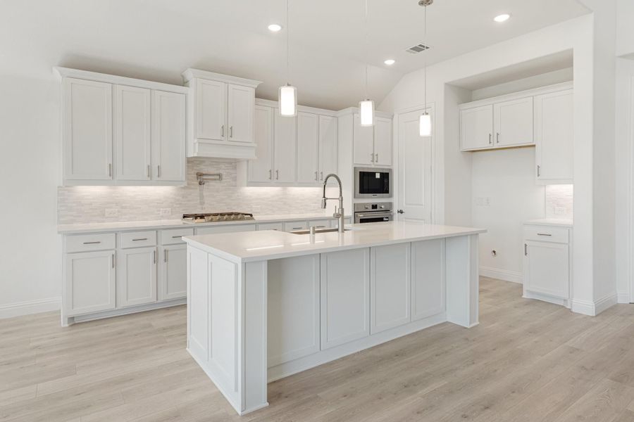 White kitchen with large center island, pendant lights, stainless appliances, tile backsplash, and light wood floors White kitchen with large center island, pendant lights, stainless appliances, tile backsplash, and light wood floors