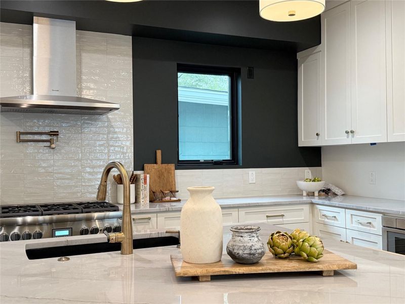Gourmet kitchen featuring a professional-grade range, stainless steel range hood, pot filler, shaker-style cabinetry, and stone countertops