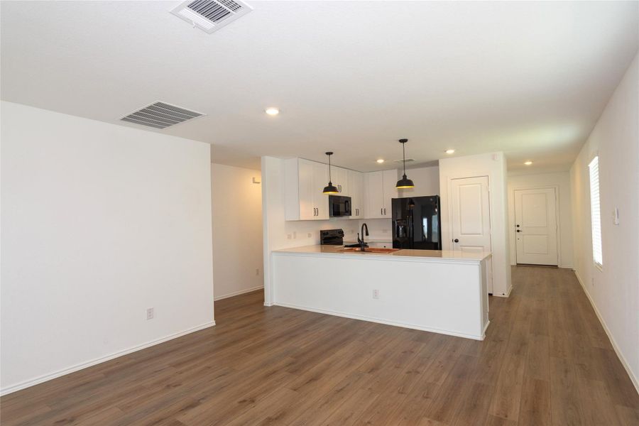 Open-concept living area featuring wood-finish flooring, white walls, and a recessed ceiling vent