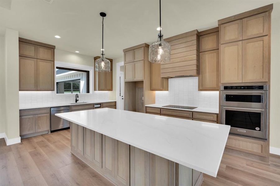 Kitchen with decorative backsplash, stainless steel appliances, a center island, and light hardwood / wood-style floors