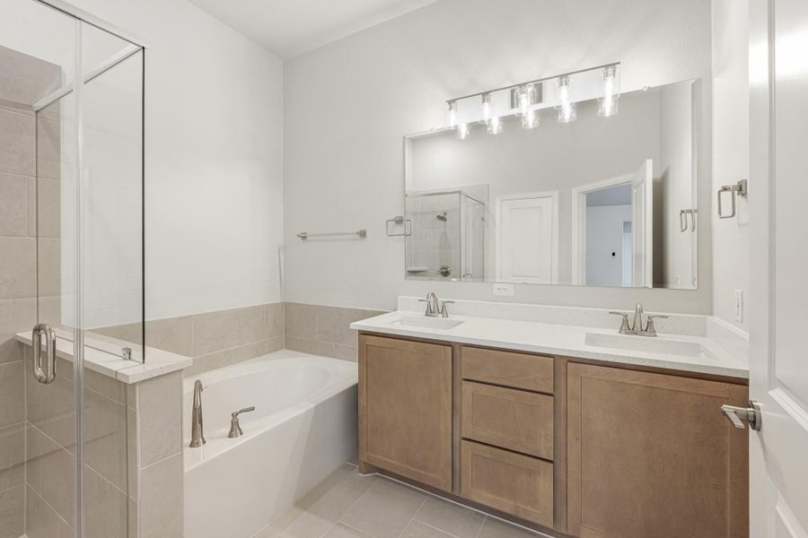 Master bathroom with double sink vanity, soaking tub, and glass walk-in shower with tile surround