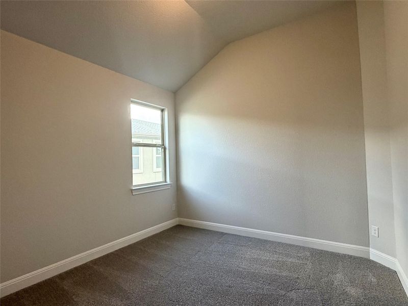 Unfurnished room featuring lofted ceiling and dark colored carpet Unfurnished room featuring lofted ceiling and dark colored carpet