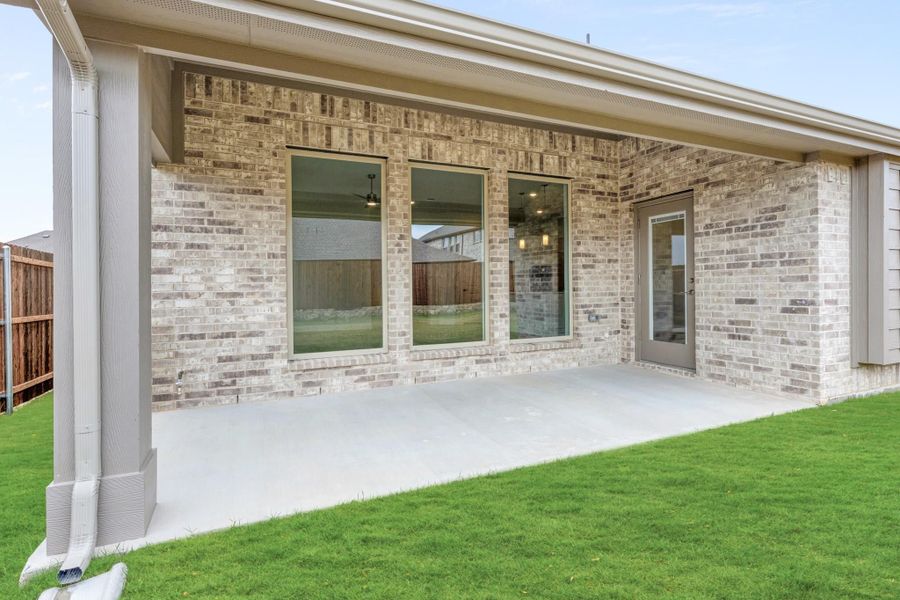 Covered back patio with concrete floor, brick exterior, large windows, and green lawn