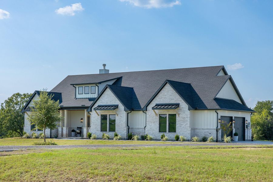 Modern farmhouse featuring a front yard, roof with shingles, a chimney, and board and batten siding