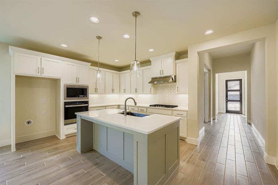 Kitchen featuring wood tiled floors, backsplash, stainless steel appliances, recessed lighting, and white cabinetry