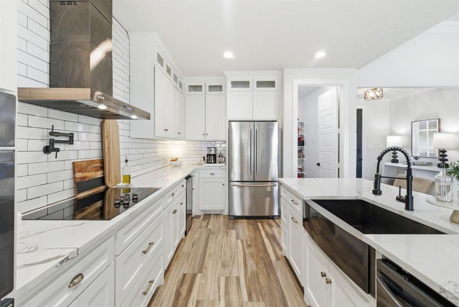 Kitchen featuring light stone counters, wall chimney range hood, light wood-type flooring, tasteful backsplash, and white cabinetry
