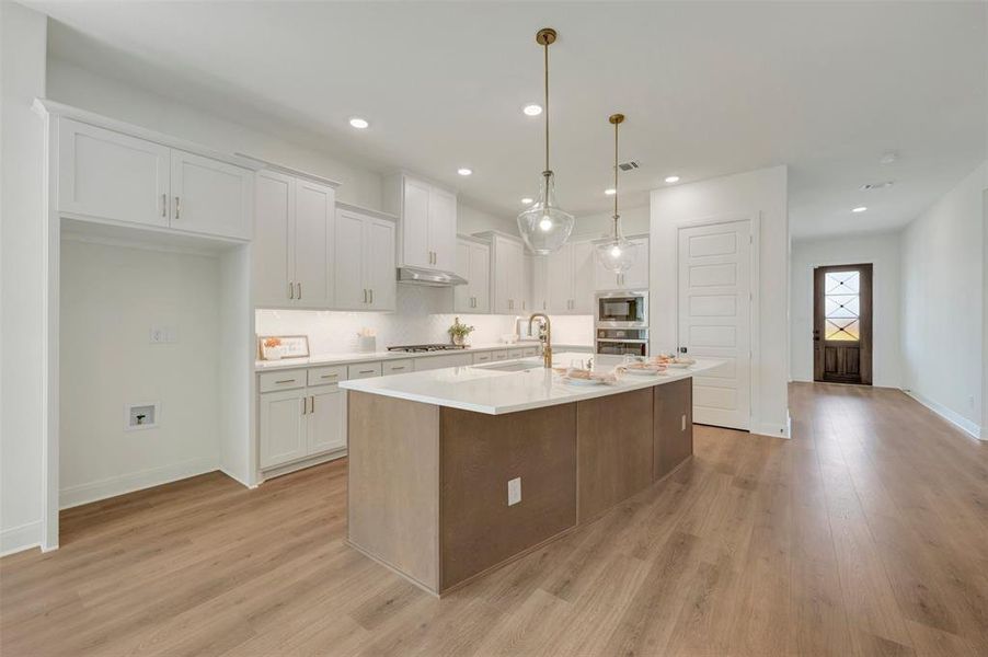 Modern kitchen featuring a large central island, white cabinetry, built-in appliances, and wood-finish flooring Modern kitchen featuring a large central island, white cabinetry, built-in appliances, and wood-finish flooring