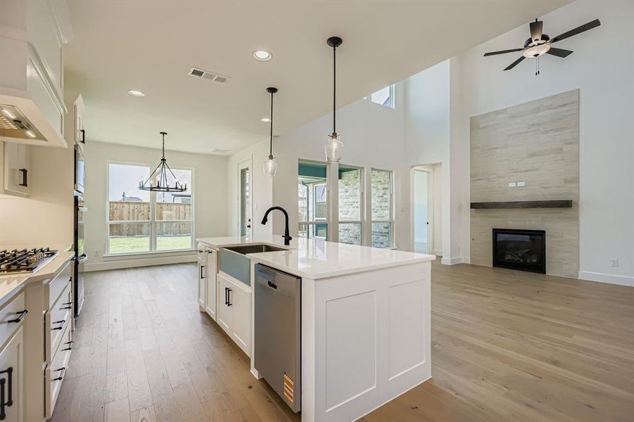 Kitchen with white cabinets, hanging light fixtures, light wood-style flooring, an island with sink, and open floor plan