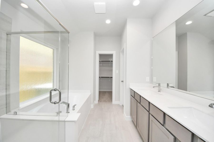 Indulge in a spa-like retreat within the confines of this primary bathroom. Delight in a spacious walk-in shower enveloped in stylish tile surround and unwind in a separate garden tub adorned with custom detailing. Sample photo of completed home with similar floor plan. Actual colors and selections may vary.