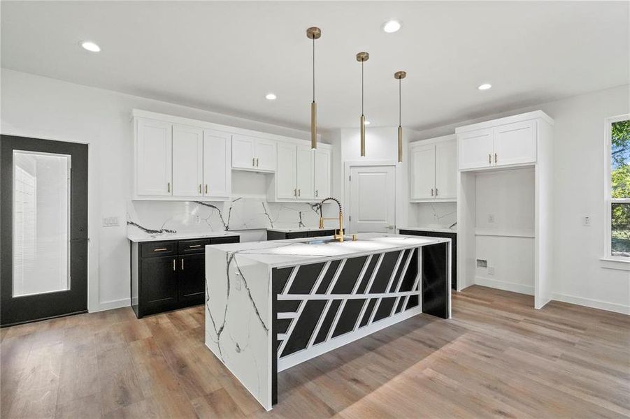 Kitchen with decorative backsplash, light wood-type flooring, pendant lighting, white cabinetry, and an island with sink