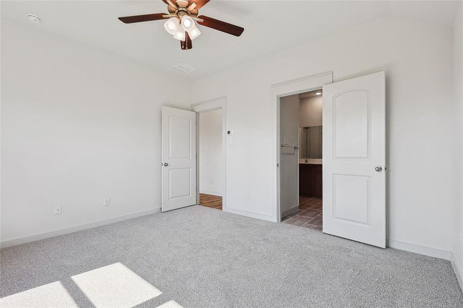 Unfurnished bedroom with ceiling fan, lofted ceiling, ensuite bath, and dark carpet