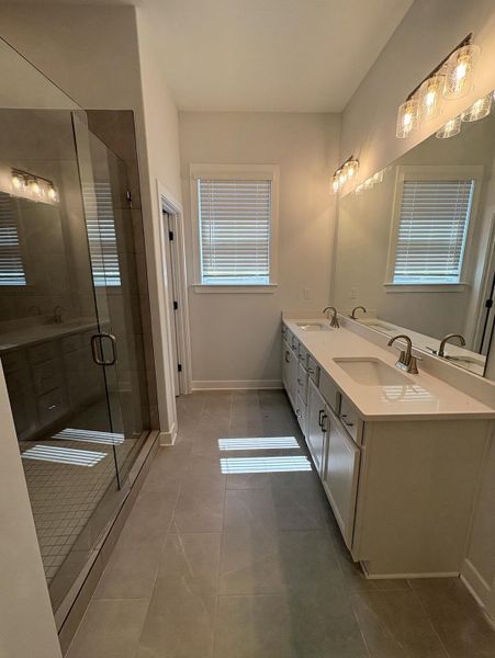 Spacious bathroom featuring a glass-enclosed shower, dual vanity with undermount sinks, stone countertops, and tile flooring