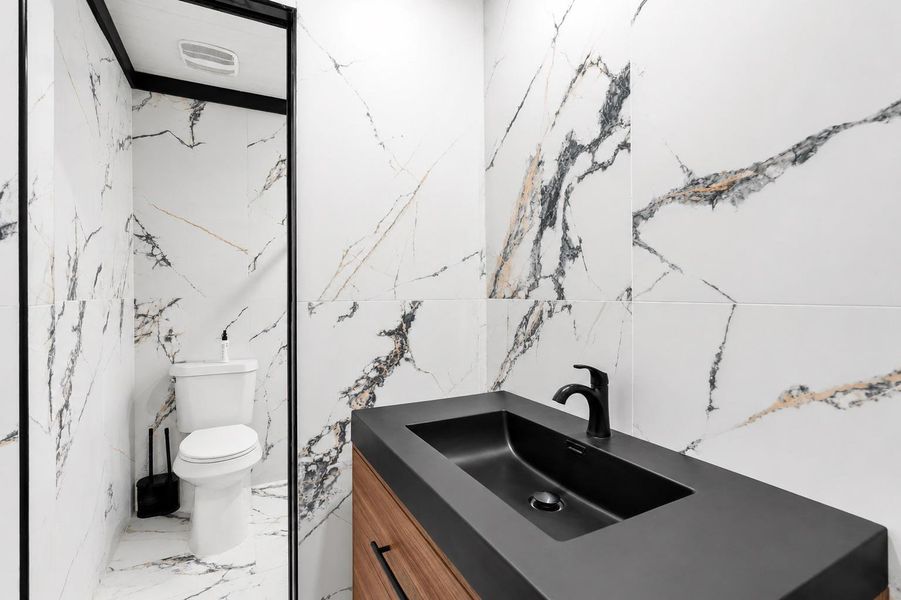 A striking powder room with sleek dark fixtures and elegant marble-patterned tile walls.