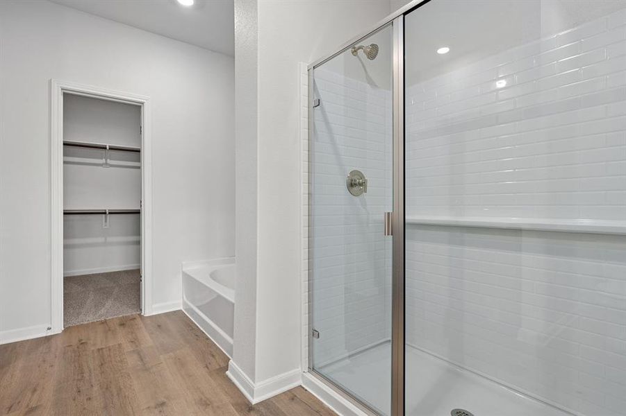 Full bathroom featuring a spacious closet, light wood finished floors, a stall shower, a garden tub, and recessed lighting Full bathroom featuring a spacious closet, light wood finished floors, a stall shower, a garden tub, and recessed lighting