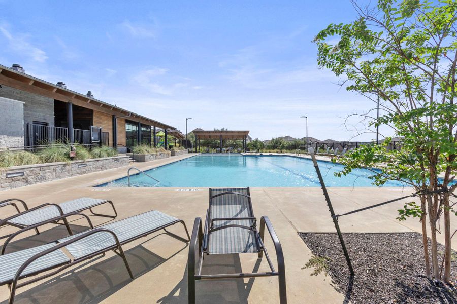 A sparkling community swimming pool sits framed by spacious concrete decking under clear blue skies.