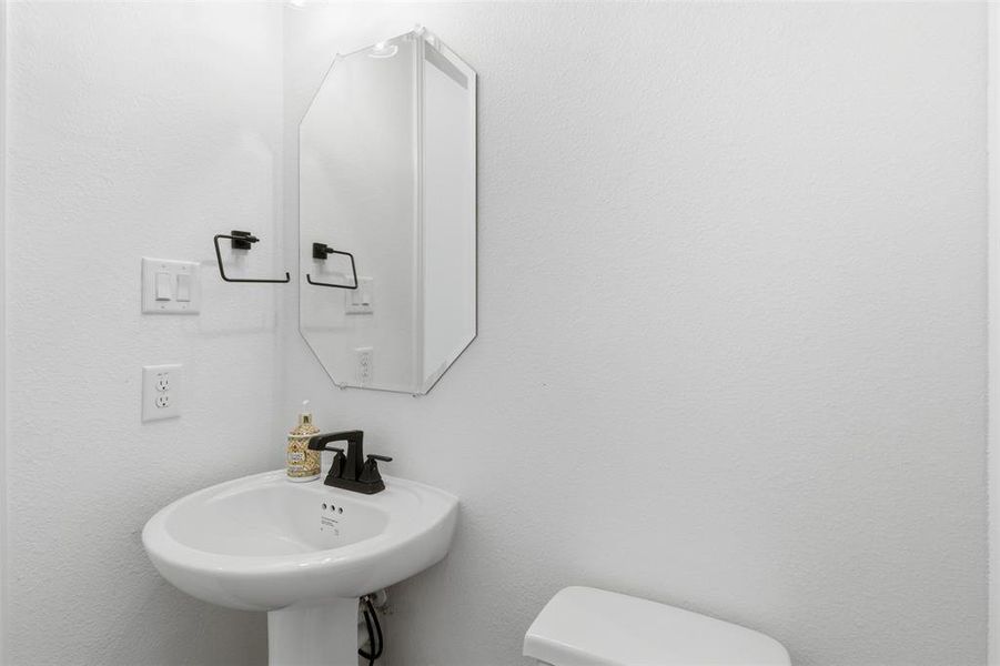 Pedestal sink with a matte black faucet and an octagonal wall-mounted mirror