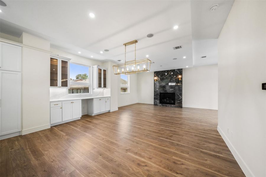 Dining area features elegant wood flooring, a modern chandelier, and a sleek black marble fireplace. Large windows provide ample natural light, and there is built-in cabinetry over dry bar for added functionality.