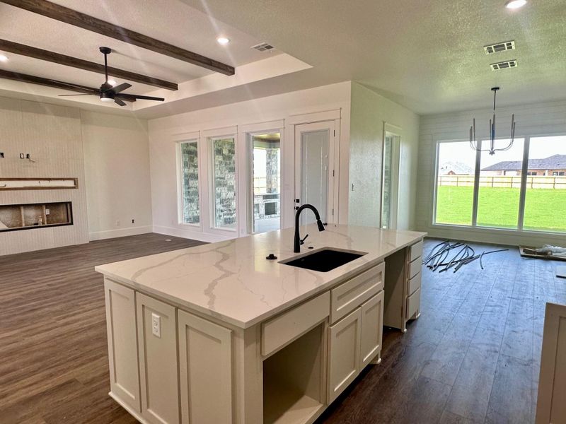 Kitchen featuring open floor plan, a large fireplace, a center island with sink, white cabinetry, and light stone counters