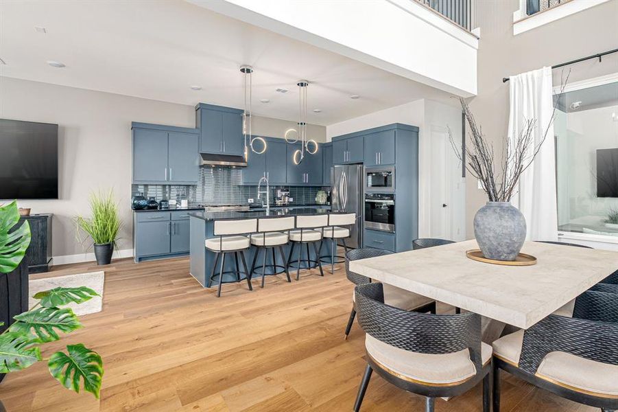 Kitchen featuring blue cabinets, a breakfast bar area, tasteful backsplash, a center island with sink, and light wood-style flooring