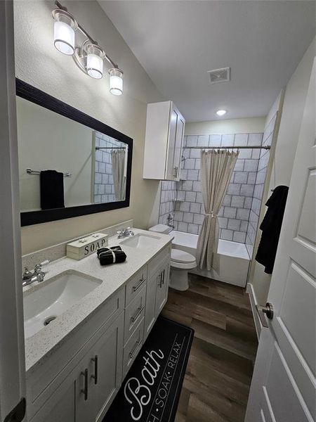 Full bathroom with luxury vinyl hardwood flooring, custom stone countertops, white shaker white soft closing cabinets vanity, custom shower / bath combination with curtain, and toilet