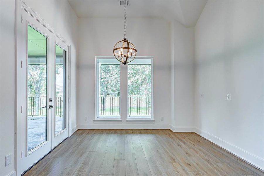 The breakfast room is ideal for circle table dining for 4 and features hardwood flooring, designer paint, a tall ceiling, a chic chandelier, easy backyard access, and bright windows.