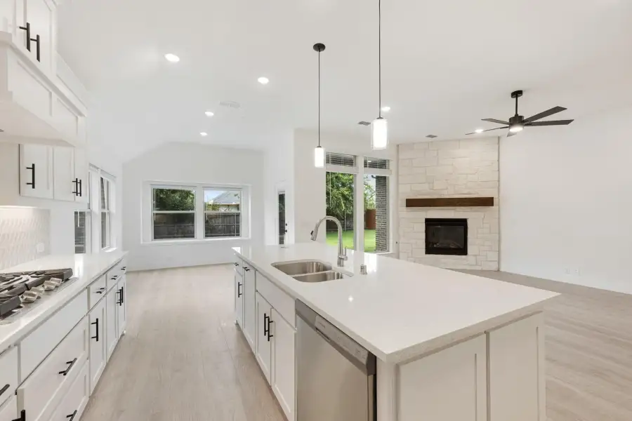 Open-concept kitchen with white cabinets, large island with sink, and stone fireplace in adjoining living area
