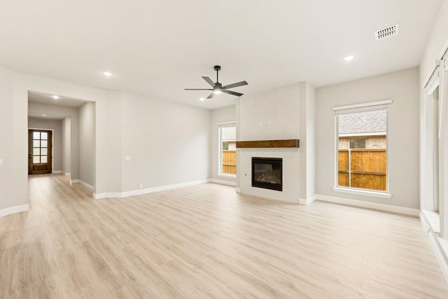 Open living room with light wood floors, fireplace with wood mantel, and ceiling fan Open living room with light wood floors, fireplace with wood mantel, and ceiling fan
