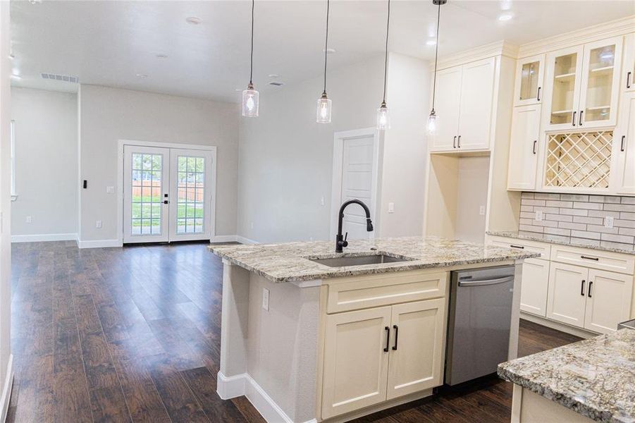 Kitchen featuring glass insert cabinets, light stone countertops, hanging light fixtures, decorative backsplash, and dark wood-style floors Kitchen featuring glass insert cabinets, light stone countertops, hanging light fixtures, decorative backsplash, and dark wood-style floors