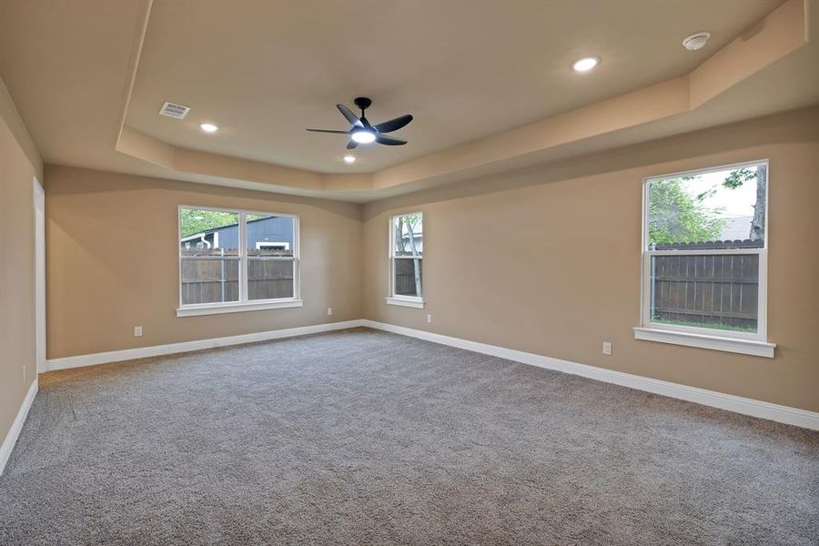 Carpeted empty room with ceiling fan, a raised ceiling, baseboards, visible vents, and recessed lighting Carpeted empty room with ceiling fan, a raised ceiling, baseboards, visible vents, and recessed lighting