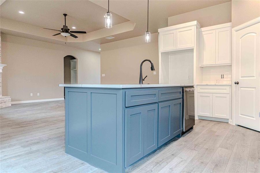 Kitchen featuring decorative light fixtures, light hardwood / wood-style flooring, a center island with sink, a tray ceiling, and white cabinets