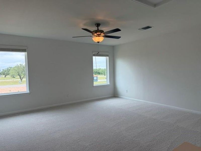 Expansive room featuring light gray carpeting, two large windows with white trim, and a ceiling fan with integrated lighting