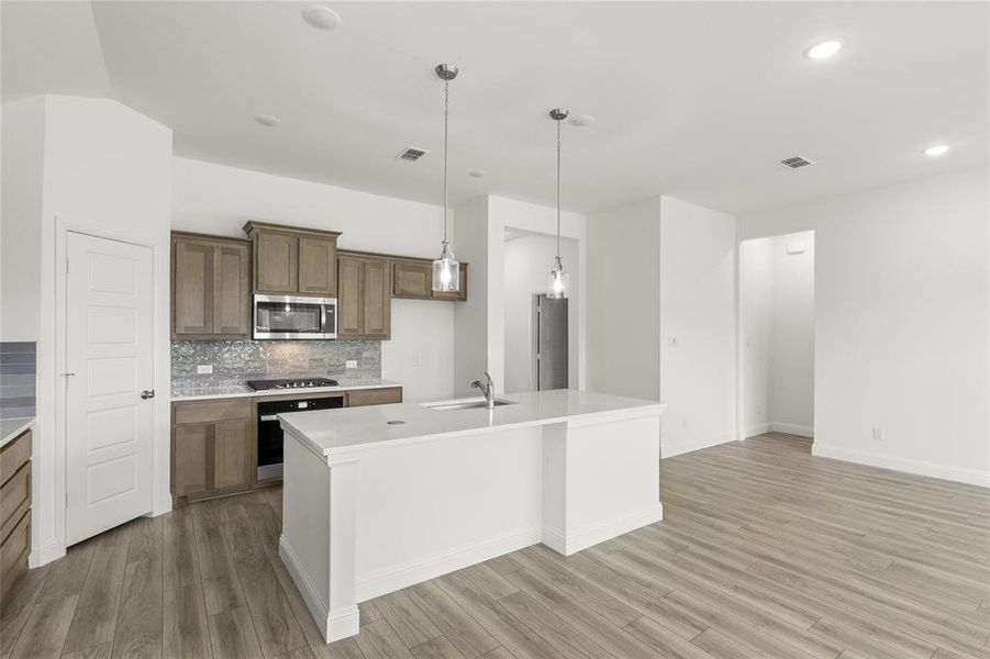 Kitchen featuring wall oven, light hardwood / wood-style flooring, tasteful backsplash, sink, and a kitchen island with sink