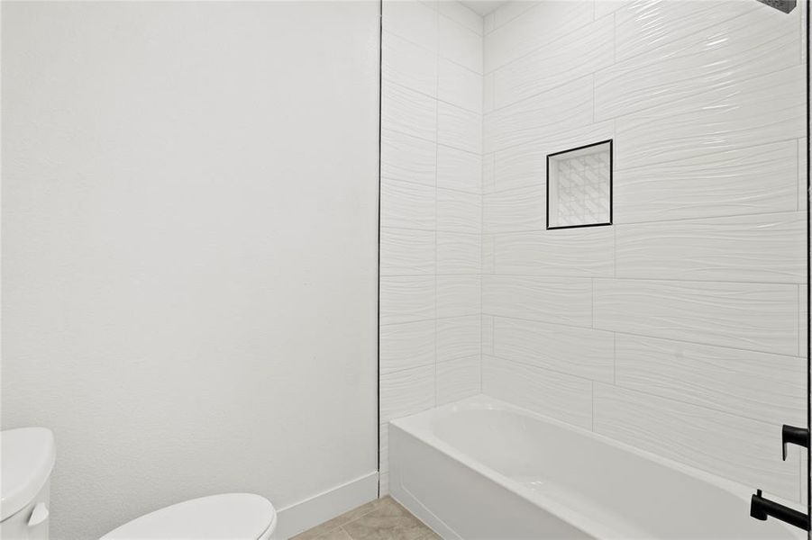 Bathroom with washtub / shower combination, tile patterned floors, and toilet