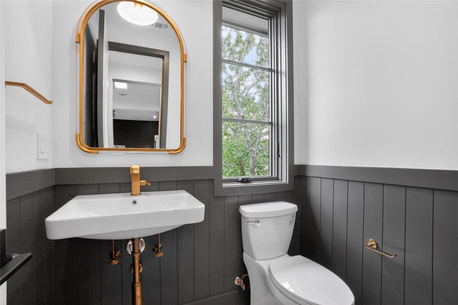 A well-lit powder room offers elegant fixtures and a window overlooking lush greenery.