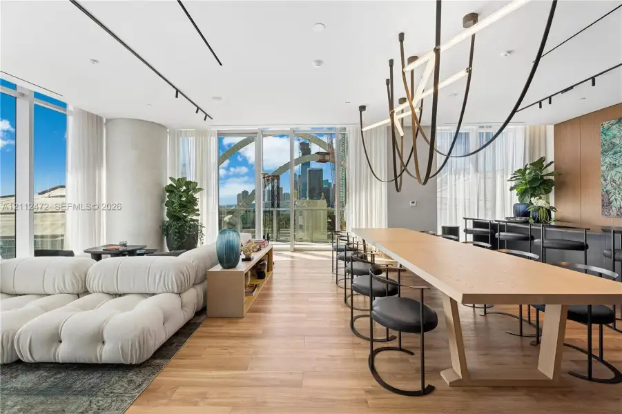 Open-concept living space featuring floor-to-ceiling windows, wood-finish flooring, custom track lighting, and a sculptural statement chandelier