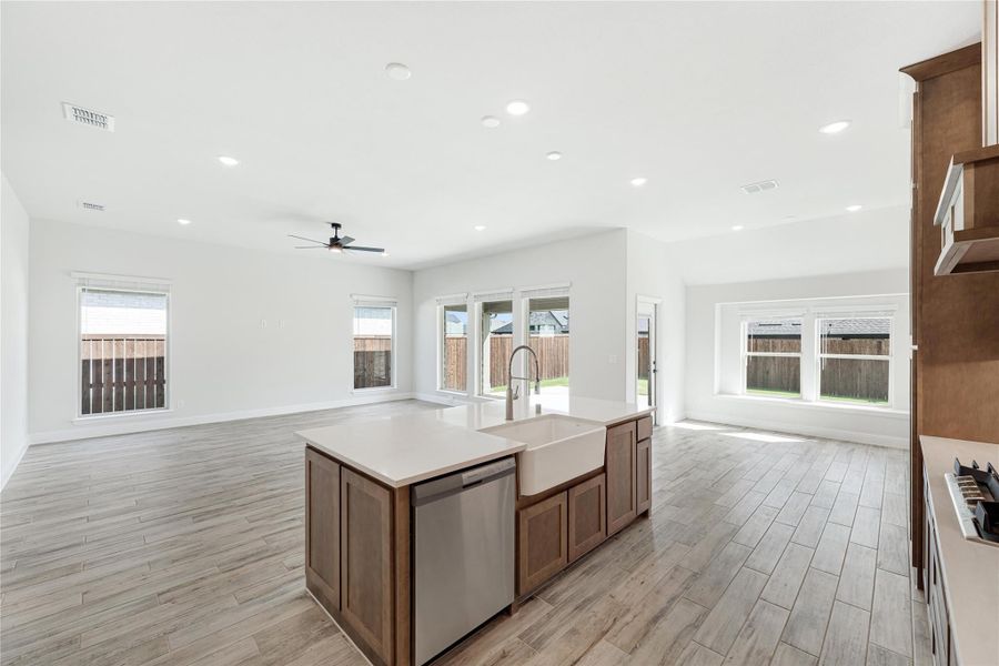 Open-concept kitchen with wood island, farmhouse sink, and dishwasher, flowing into a bright living area with wood-look floors