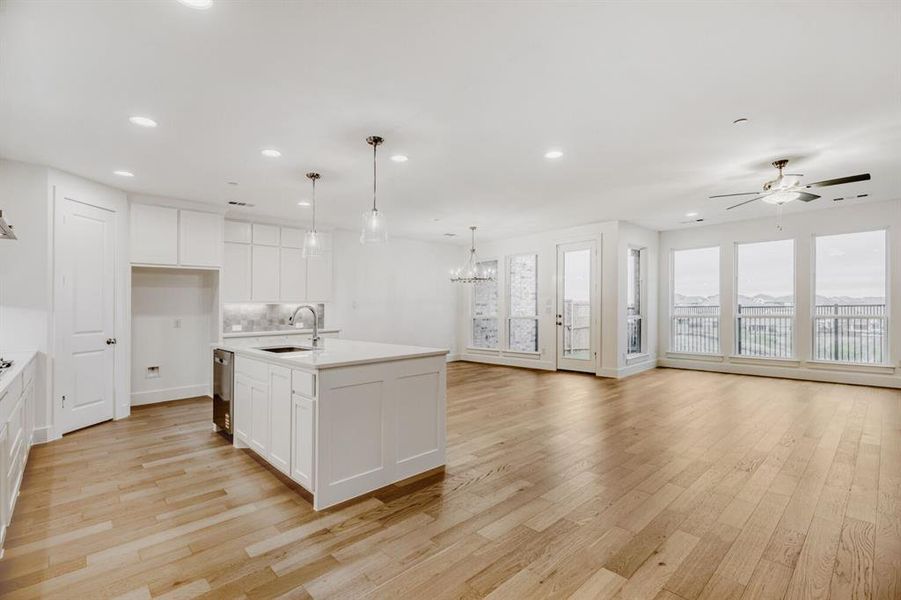 Expansive open-concept living space featuring wood-finish flooring throughout, a modern kitchen island with integrated sink, stainless steel dishwasher, white cabinetry, and recessed lighting