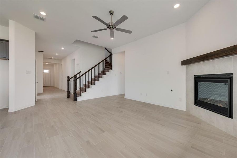 Unfurnished living room featuring ceiling fan, light wood-type flooring, and a tiled fireplace