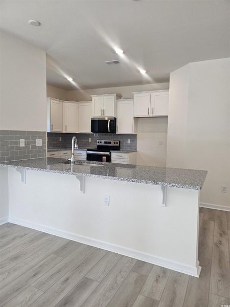 Kitchen featuring a kitchen bar, light stone counters, white cabinetry, decorative backsplash, and appliances with stainless steel finishes