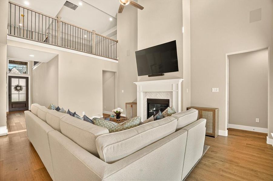 Spacious living area featuring a two-story ceiling, wood-finish flooring, and a fireplace with a white mantel and herringbone tile surround Spacious living area featuring a two-story ceiling, wood-finish flooring, and a fireplace with a white mantel and herringbone tile surround