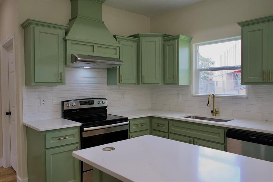 Kitchen with green cabinets, stainless steel appliances, decorative backsplash, and custom range hood