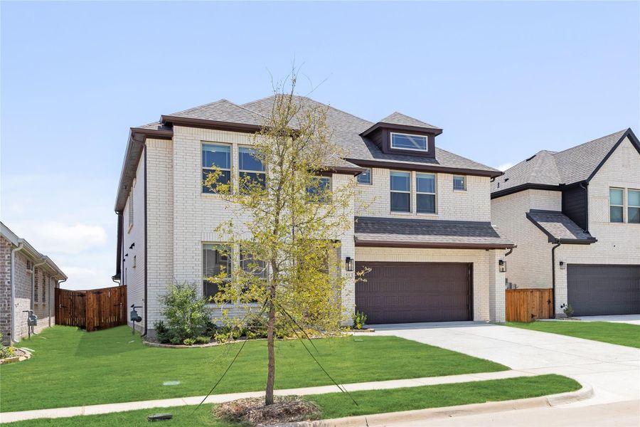 Two-story brick home with two-car garage, dormer window, and manicured front lawn