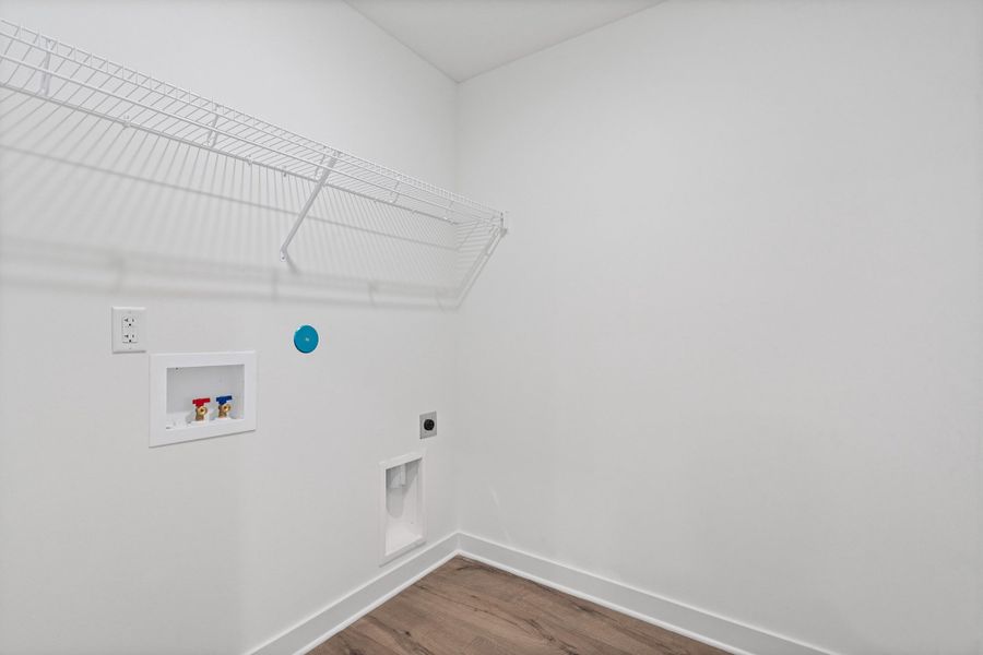 Laundry area featuring a white wire shelving unit, appliance hookups, and wood-finish flooring Laundry area featuring a white wire shelving unit, appliance hookups, and wood-finish flooring