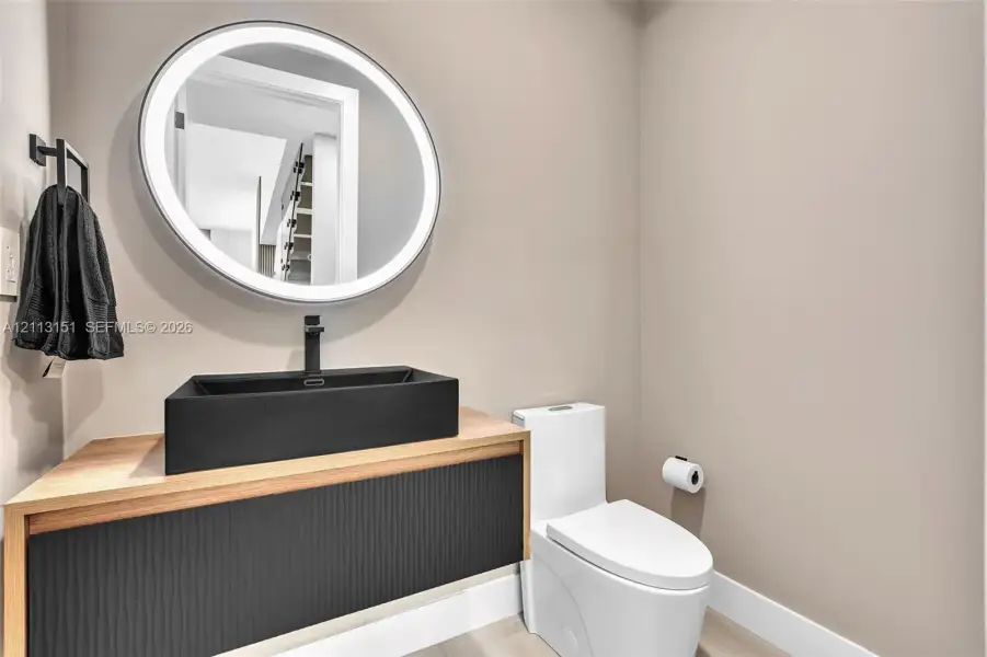 Floating vanity featuring a wood-tone countertop, matte black rectangular vessel sink, and textured black cabinetry, paired with an oval LED-backlit mirror and matte black wall-mounted faucet Floating vanity featuring a wood-tone countertop, matte black rectangular vessel sink, and textured black cabinetry, paired with an oval LED-backlit mirror and matte black wall-mounted faucet