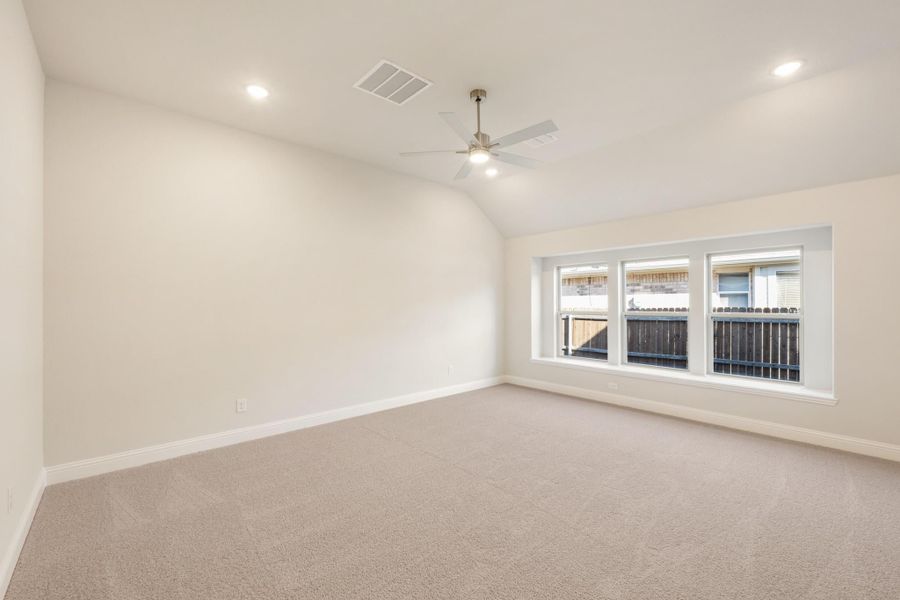 Empty bedroom with vaulted ceiling, ceiling fan, carpet flooring, and large triple window Empty bedroom with vaulted ceiling, ceiling fan, carpet flooring, and large triple window