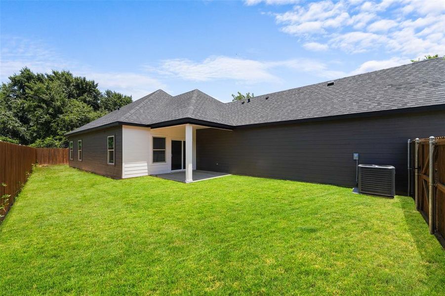 Expansive green lawn surrounding a modern residence with dark siding and a covered patio Expansive green lawn surrounding a modern residence with dark siding and a covered patio