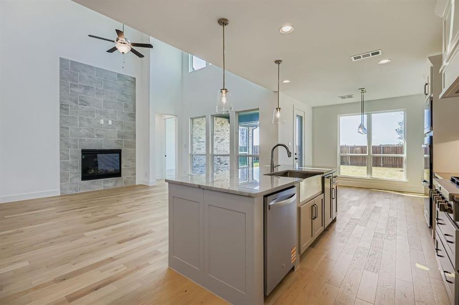 Kitchen featuring hanging light fixtures, healthy amount of natural light, a kitchen island with sink, light stone counters, and recessed lighting Kitchen featuring hanging light fixtures, healthy amount of natural light, a kitchen island with sink, light stone counters, and recessed lighting