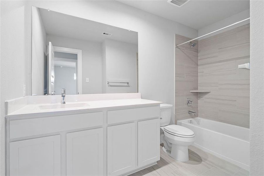 Secondary bath features tile flooring, bath/shower combo with tile surround, white stained wood cabinets, beautiful light countertops, mirror, dark, sleek fixtures and modern finishes.