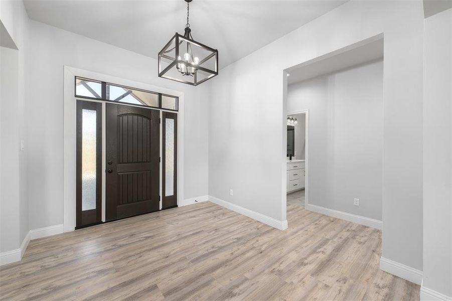 Entrance foyer with light wood finished floors, baseboards, and a notable chandelier